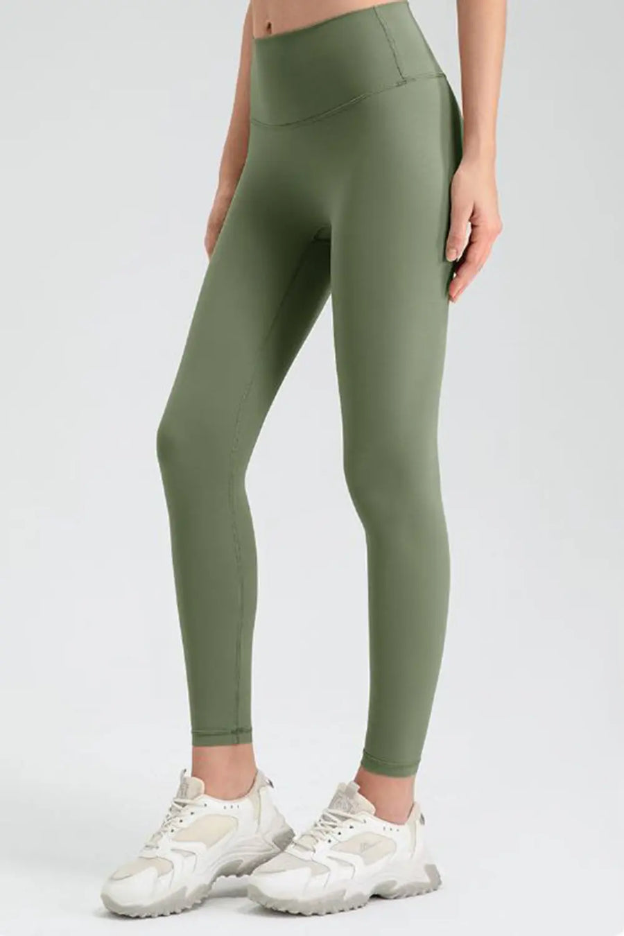 Person wearing olive green leggings with white sneakers on a light gray background
