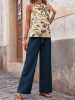 Woman wearing a floral top and blue pants standing against a textured wall.