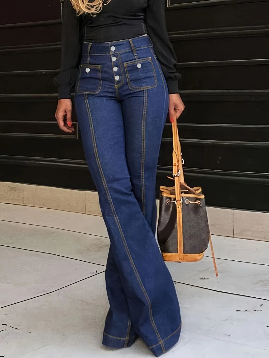 Person wearing blue flared jeans with a black top and holding a brown handbag.