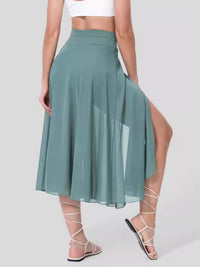 Person wearing a green skirt with a slit on a plain background