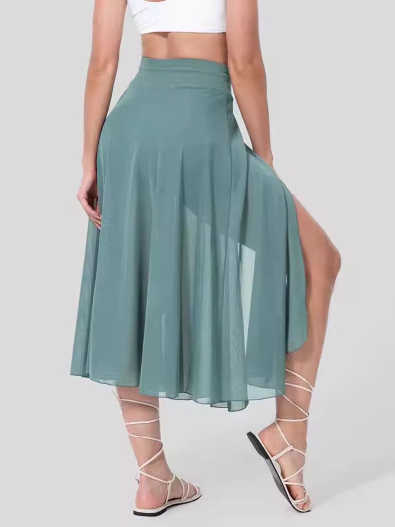 Person wearing a green skirt with a slit on a plain background