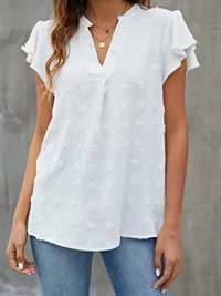 Woman wearing a white blouse with ruffled sleeves against a gray background