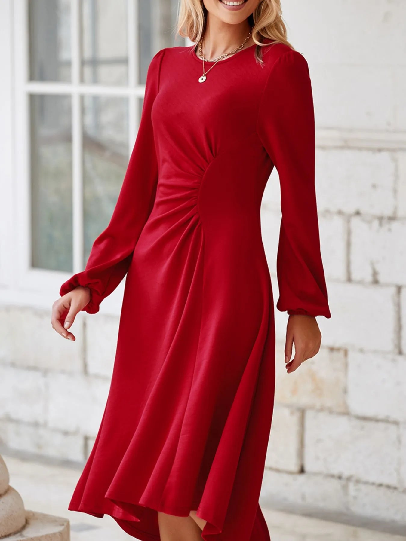 Woman wearing a red dress with long sleeves in an outdoor setting.