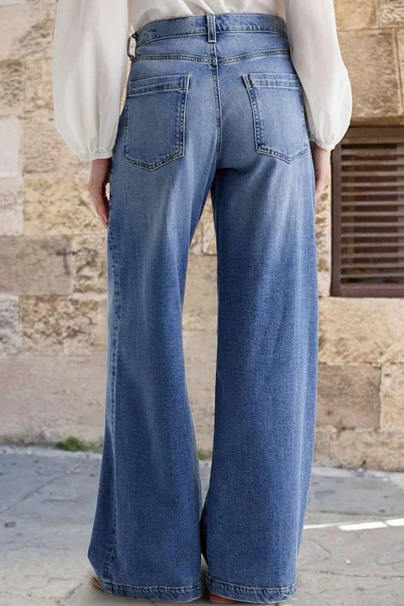 Person wearing blue wide-leg jeans standing against a stone wall.