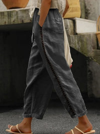 Person wearing dark gray wide-leg pants with decorative stitching, standing on a textured surface.