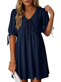 Navy blue dress with puff sleeves and tie details on a white background