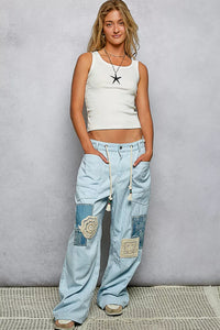 Woman wearing a white tank top and patchwork jeans against a gray background