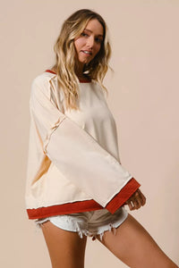 Woman wearing a white and red long-sleeve top with denim shorts on a beige background