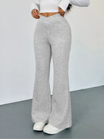 Person wearing gray flared pants and a white top on a plain background