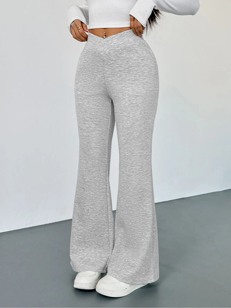 Person wearing gray flared pants and a white top on a plain background