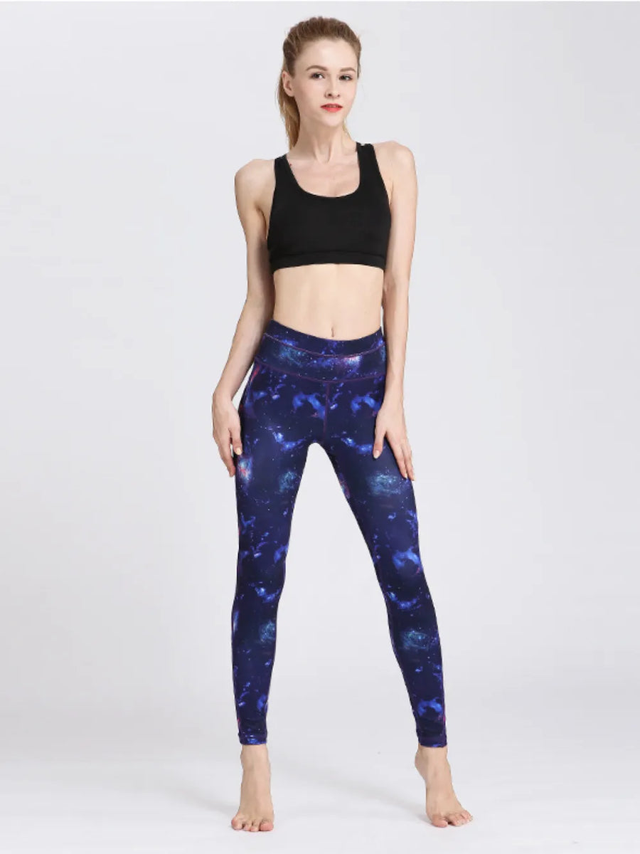 Woman wearing black sports bra and blue galaxy leggings on a white background