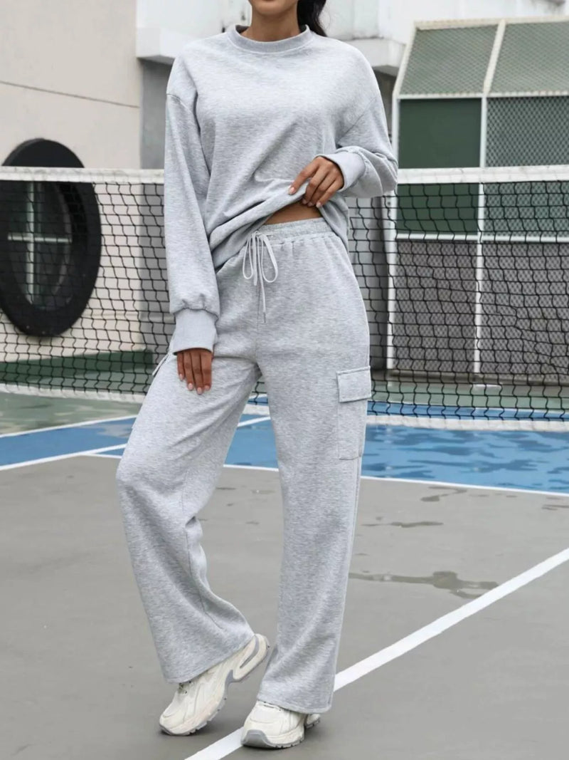 Person wearing a gray sweatshirt and pants on a tennis court