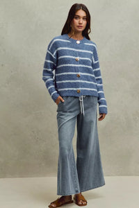 Woman wearing a blue and white striped sweater and jeans against a neutral background