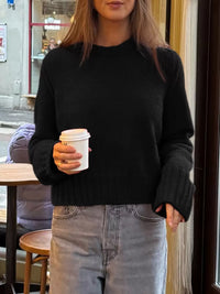 Person wearing a black sweater and holding a coffee cup in an urban setting