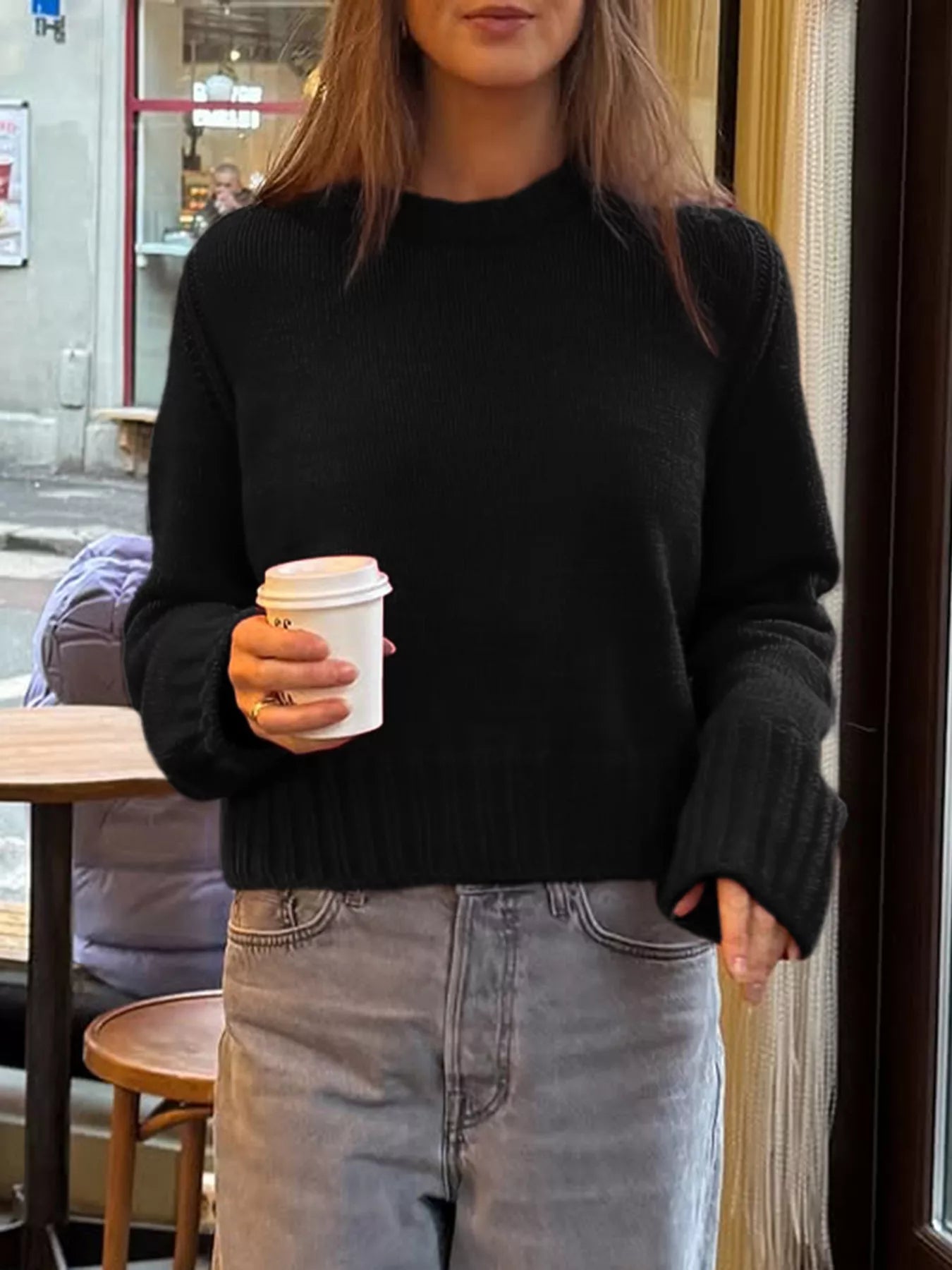 Person wearing a black sweater and holding a coffee cup in an urban setting
