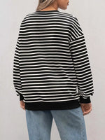 Person wearing a black and white striped sweater with light blue jeans on a plain background