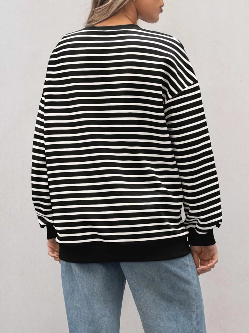 Person wearing a black and white striped sweater with light blue jeans on a plain background