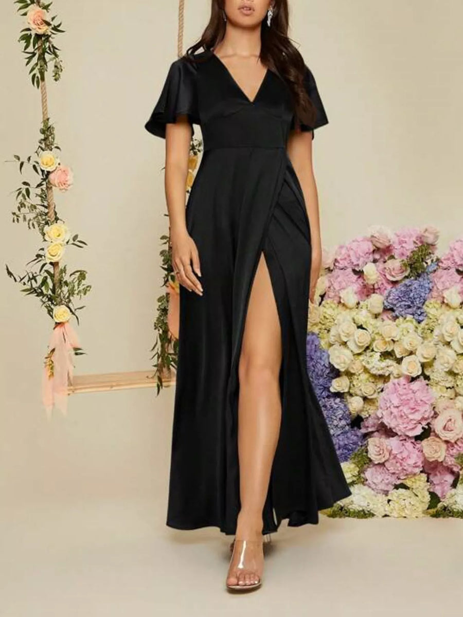 Woman wearing a black dress with a slit in front, standing against a floral background.