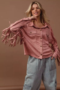 Woman wearing a pink fringed jacket and light blue jeans against a brown background