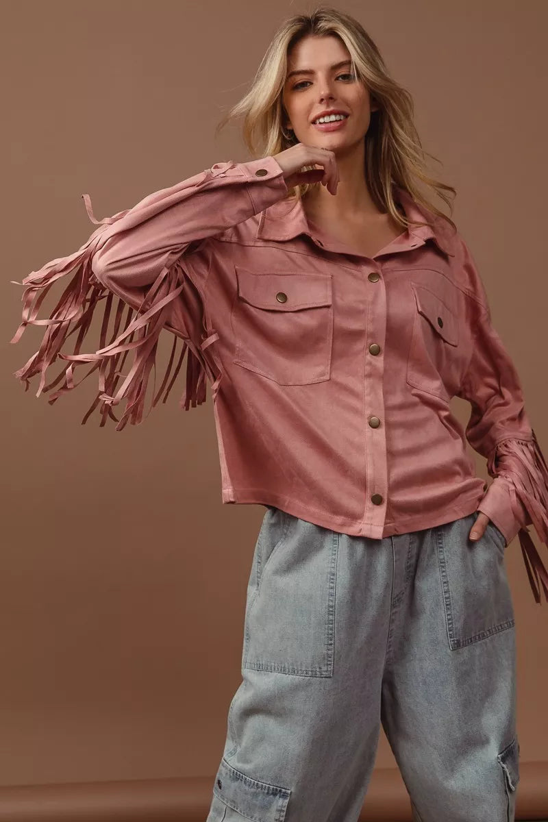 Woman wearing a pink fringed jacket and light blue jeans against a brown background
