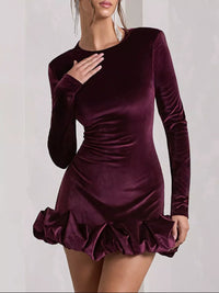 Purple velvet dress with long sleeves and ruffled skirt on a plain background
