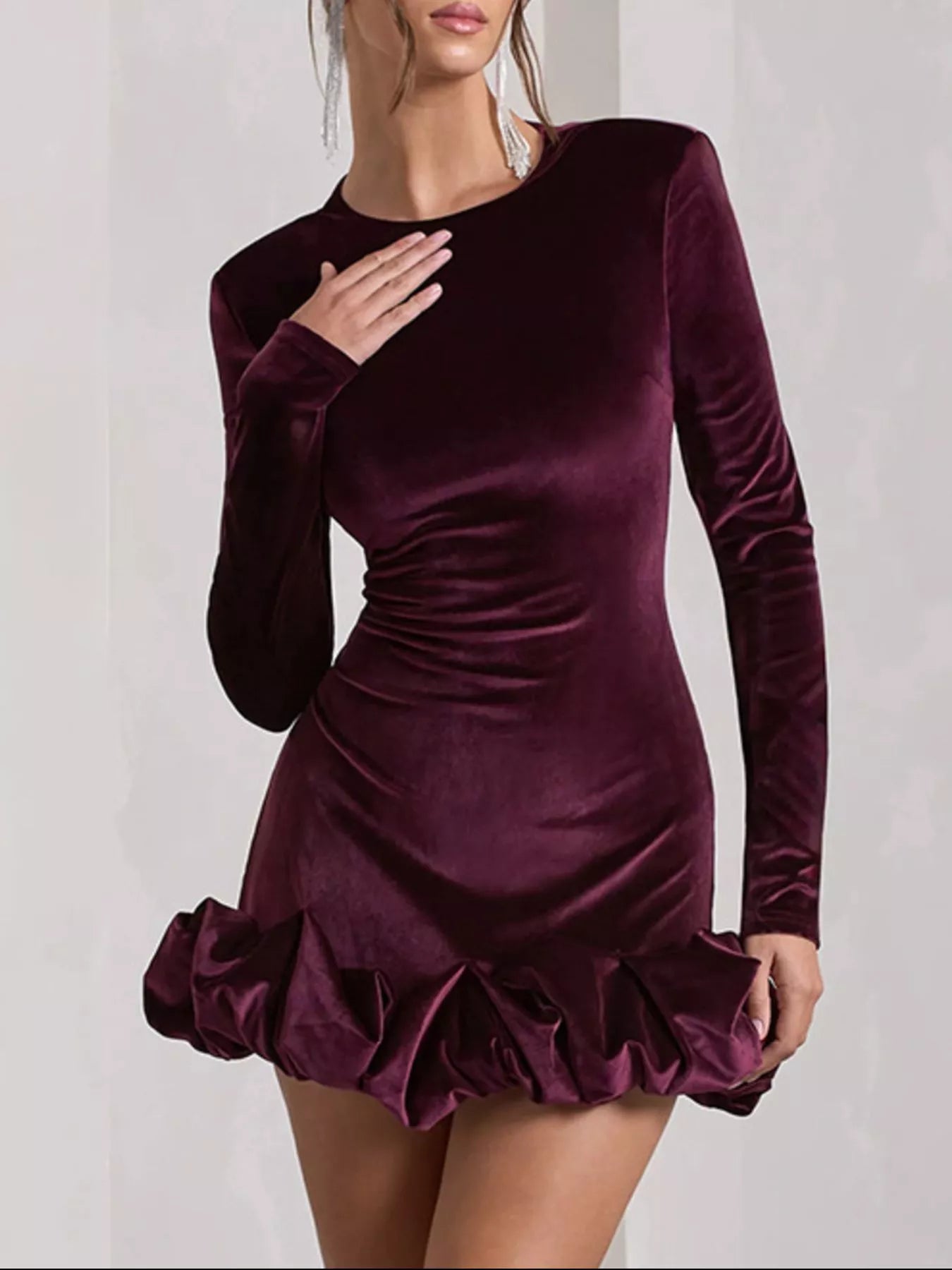 Purple velvet dress with long sleeves and ruffled skirt on a plain background