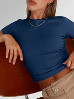 Woman wearing a blue top and beige pants sitting on a wooden chair.