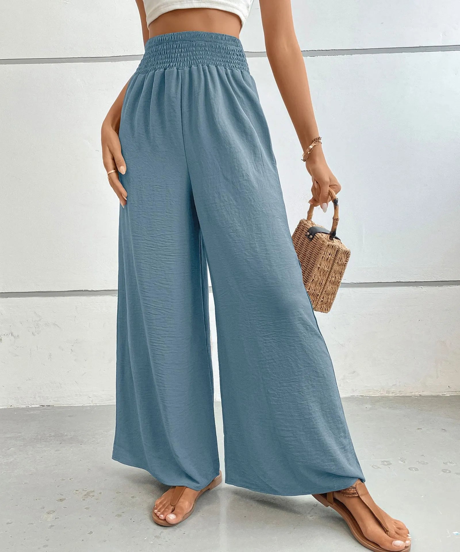 Person wearing blue wide-leg pants holding a woven bag against a white background