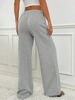 Person wearing gray wide-leg pants against a white wall.