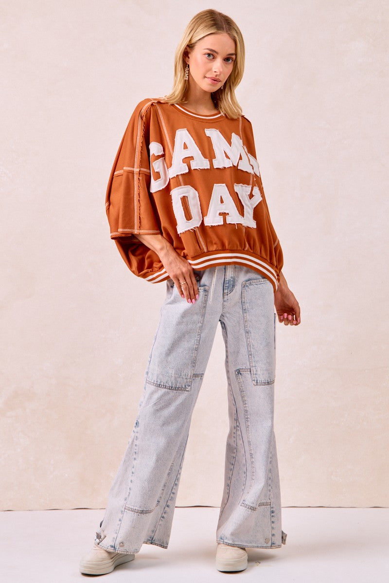 Woman wearing a 'GAMEDAY' sweater and light blue jeans on a plain background