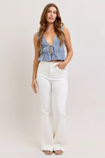 Woman wearing a checkered top and white pants against a plain background