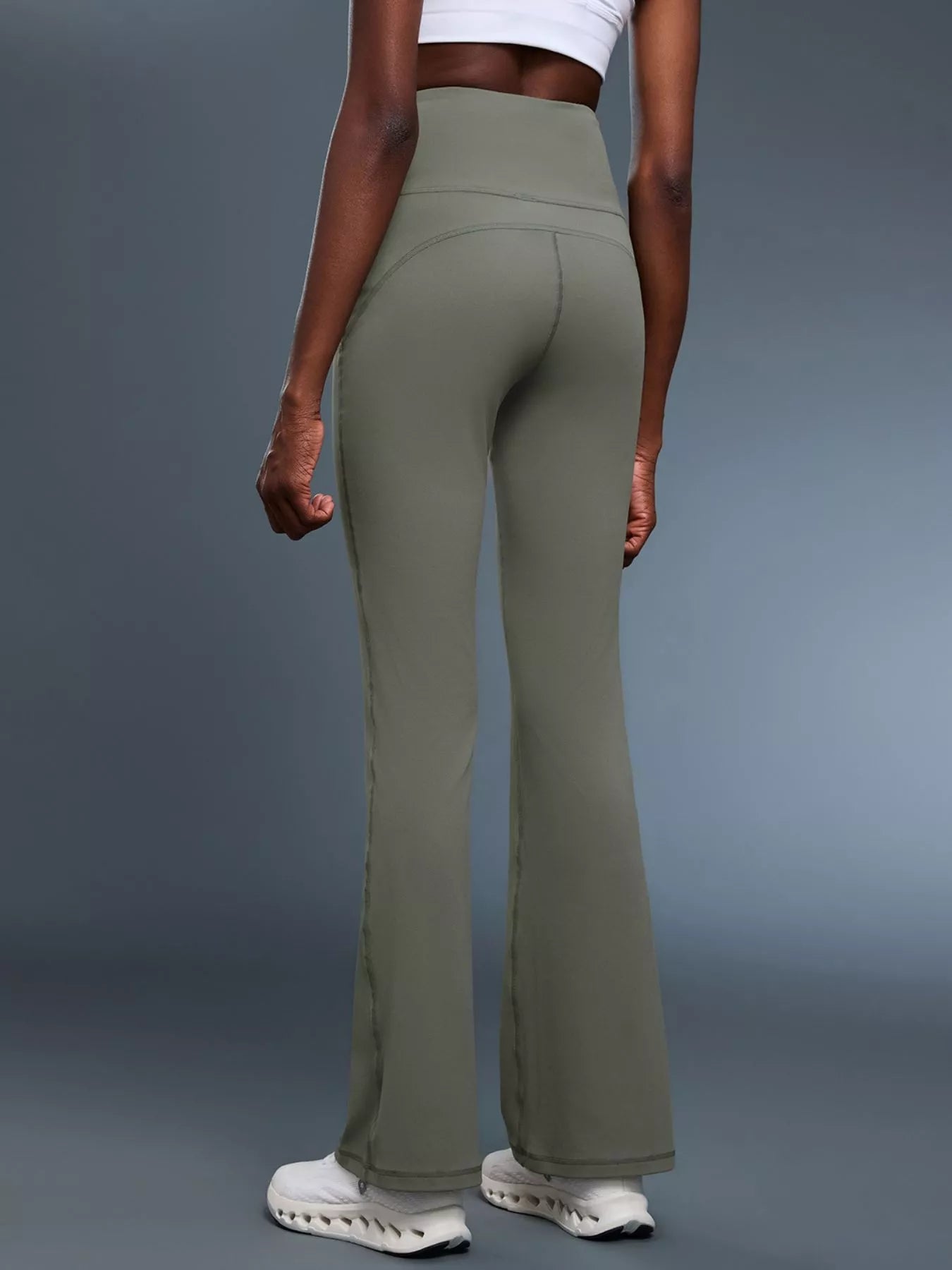 Person wearing olive green flared pants on a gray background