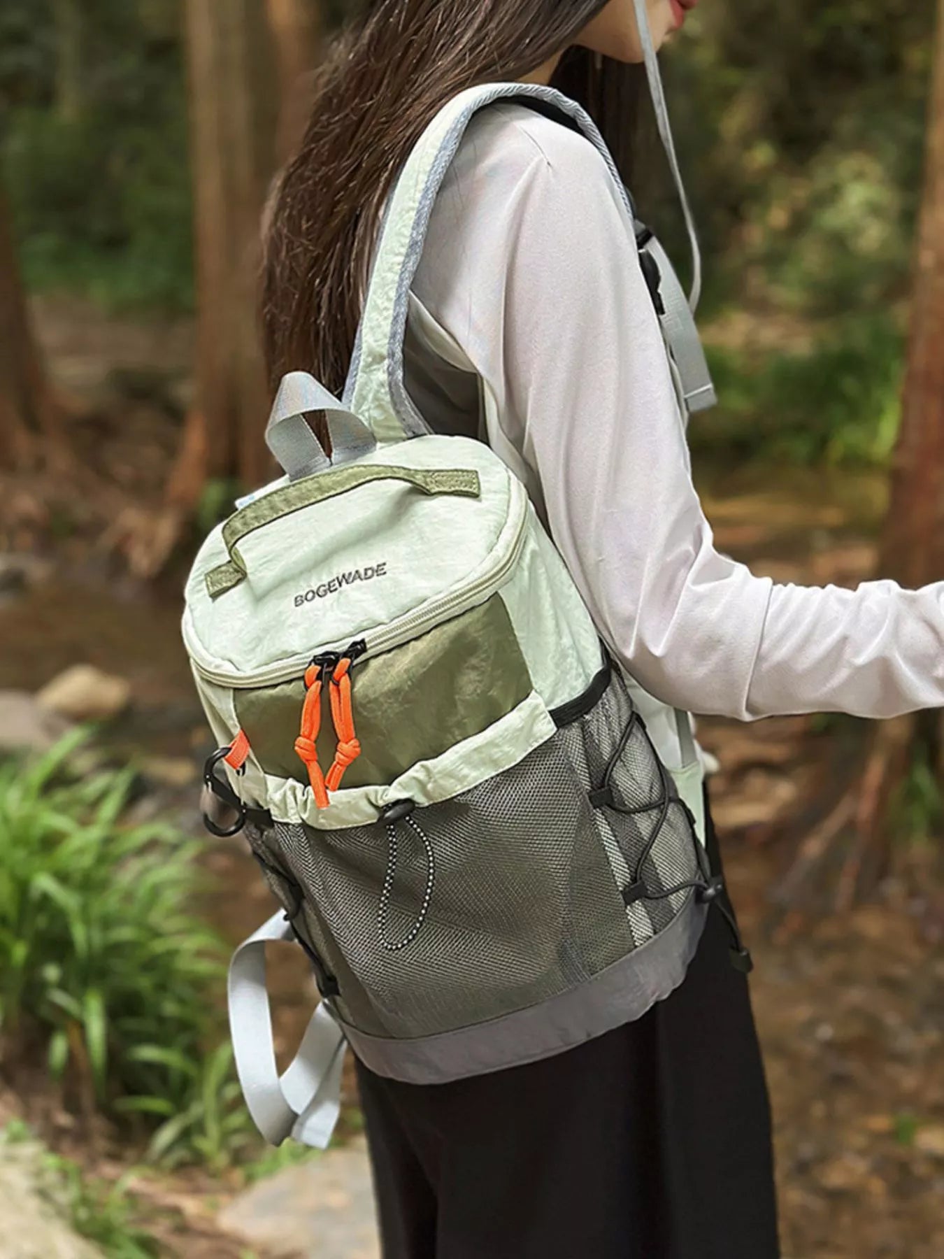 Person wearing a green and gray backpack with orange accents in a forest setting