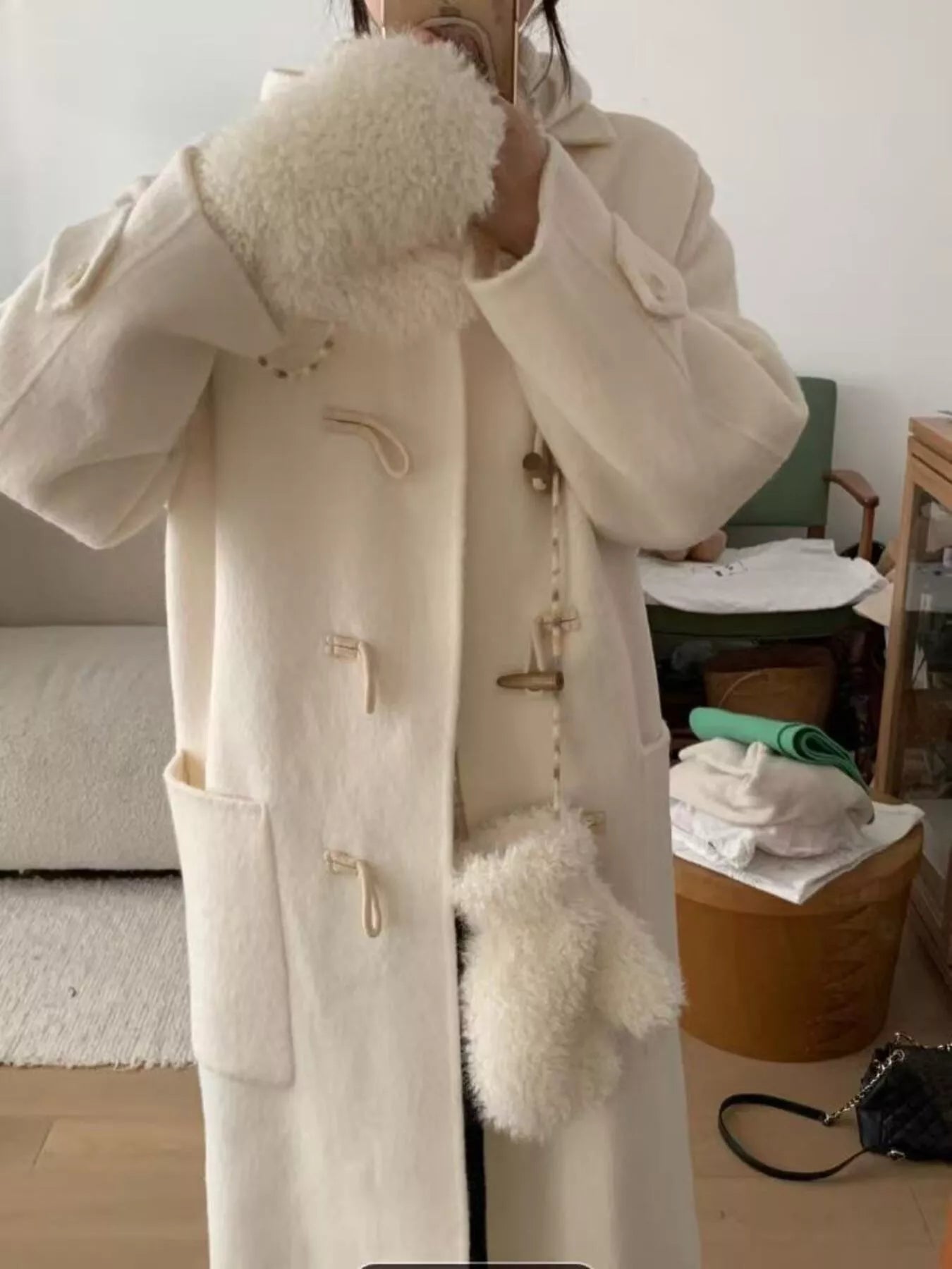Person wearing a long beige coat with fur trim in a room.