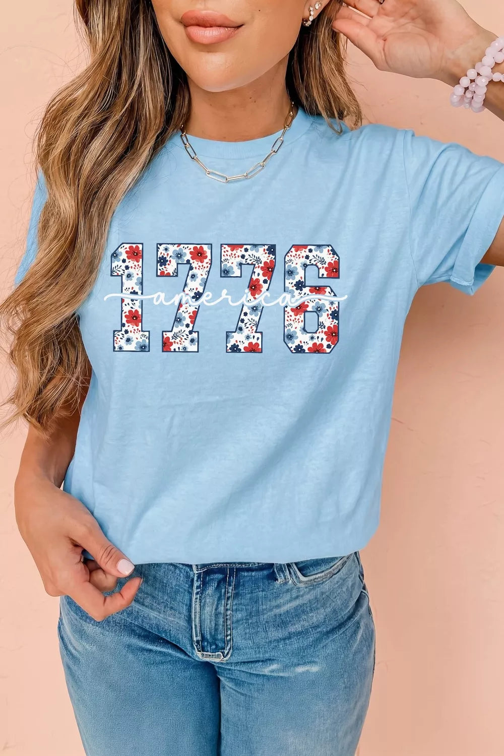 Person wearing a light blue t-shirt with '1776' printed on it, standing against a beige background.