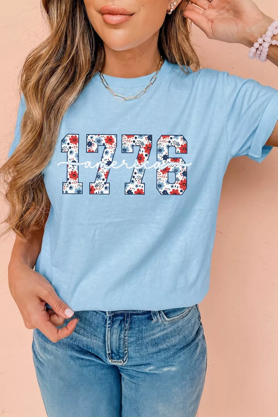 Person wearing a light blue t-shirt with '1776' printed on it, standing against a beige background.
