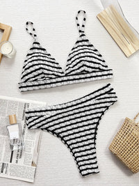 Black and white striped bikini set on a light surface with a candle and newspaper.