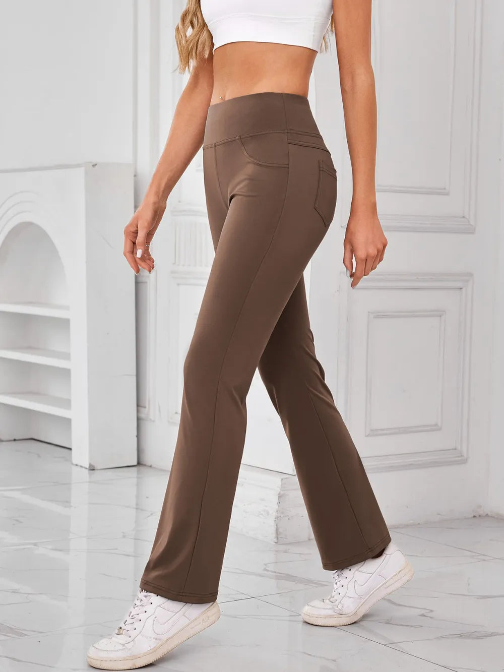 Person wearing brown flared pants and white sneakers in a minimalistic setting