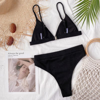 Black bikini set on a textured surface with a magazine and decorative elements.
