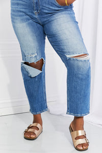 Ripped blue jeans worn by a person on a white background