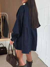Person wearing a navy blue dress with long sleeves and a brown handbag indoors.