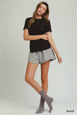 Woman wearing a black t-shirt and gray shorts on a plain background