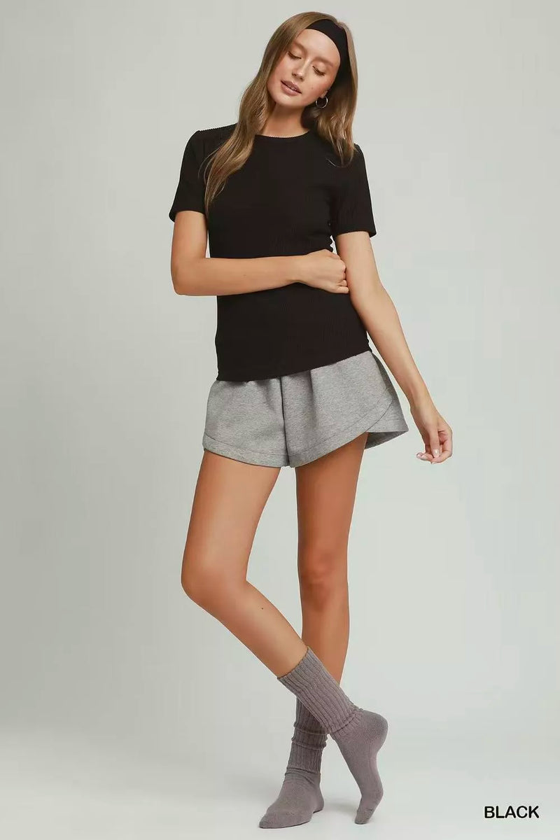 Woman wearing a black t-shirt and gray shorts on a plain background