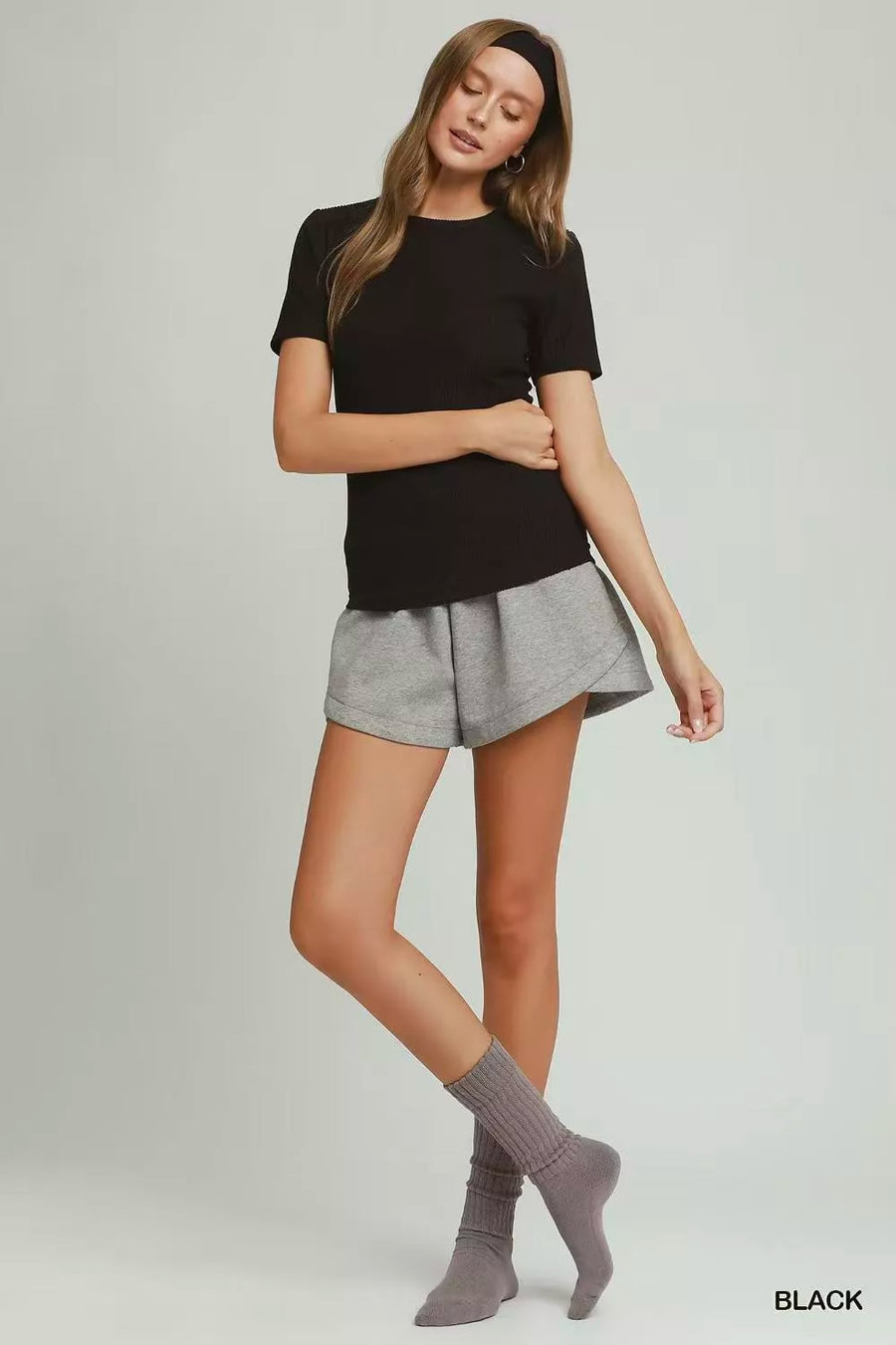 Woman wearing a black t-shirt and gray shorts on a plain background