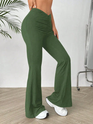 Green flared pants worn by a person on a wooden floor with a white wall background