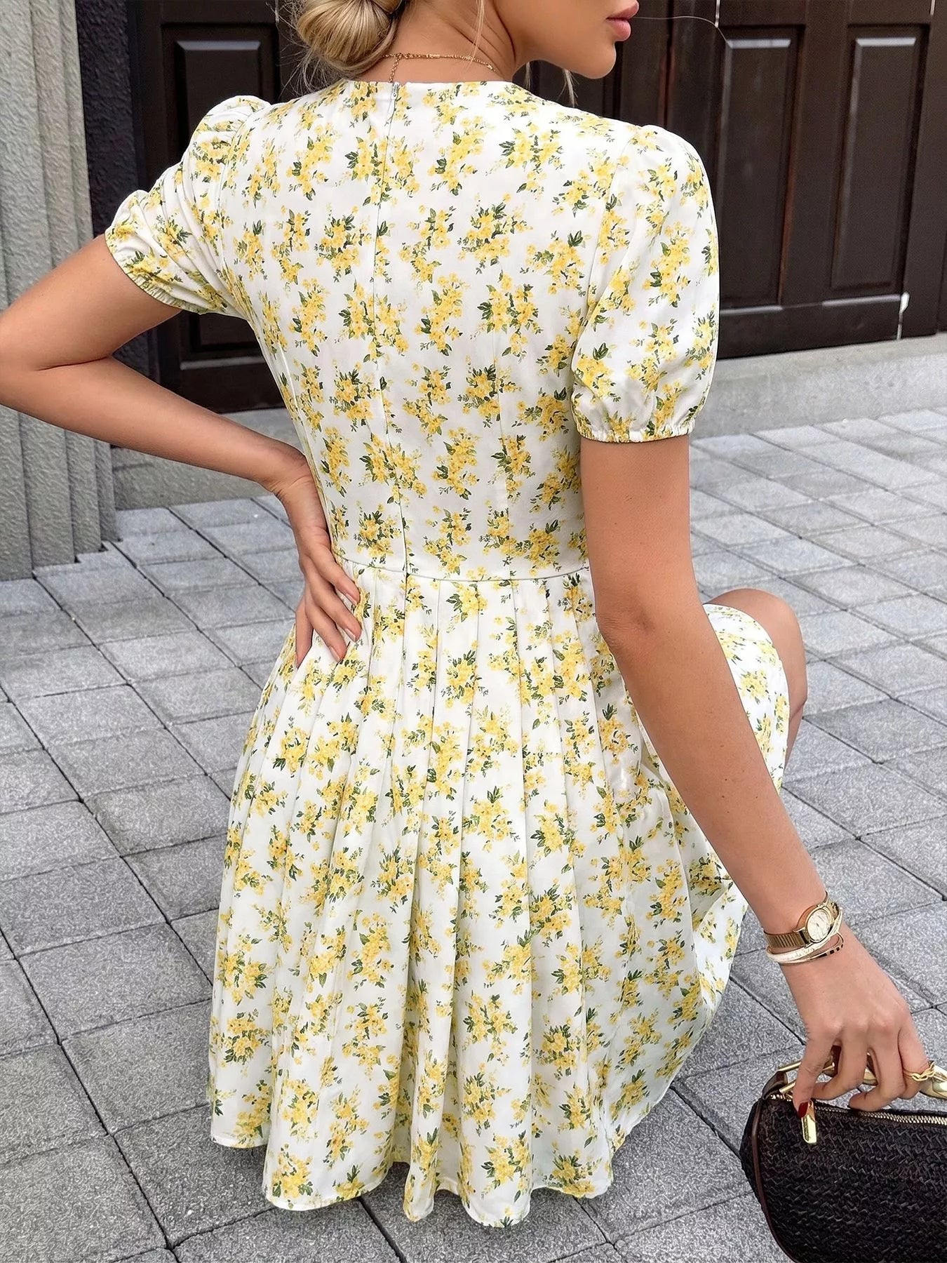 Woman wearing a white dress with yellow floral pattern on a paved walkway.