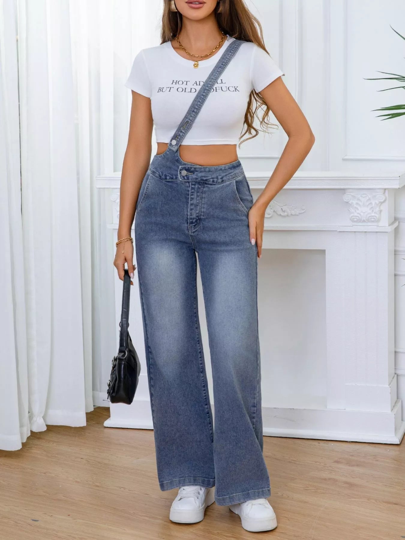 Woman wearing a white crop top and blue jeans with a black handbag indoors.