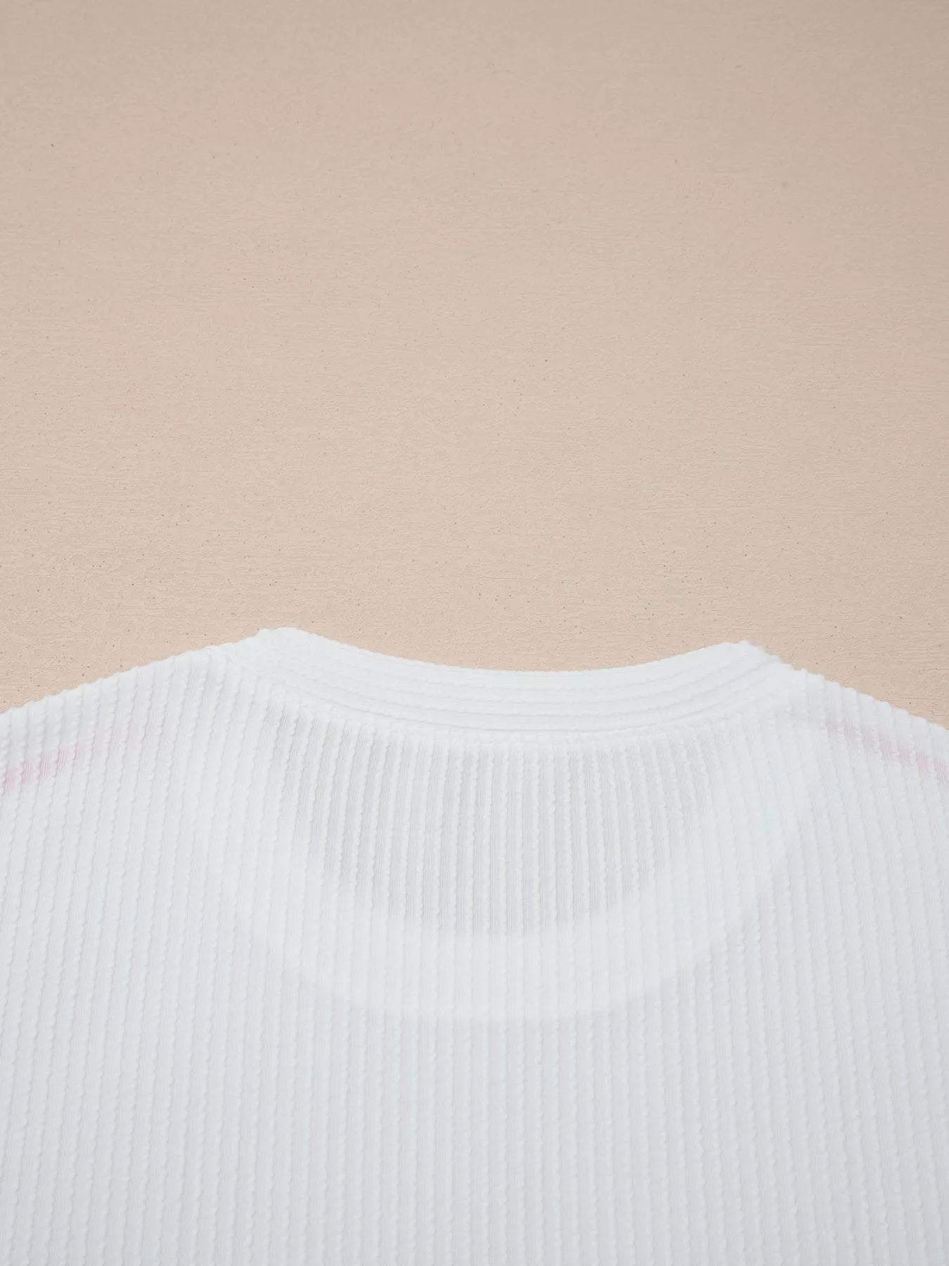 Close-up of a white ribbed sweater on a beige background