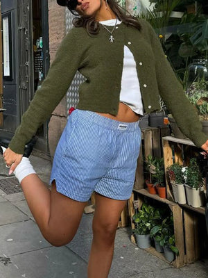 Person wearing a green cardigan, white top, and blue shorts on a street.