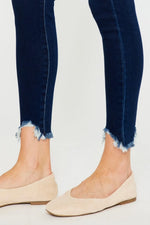 Navy blue jeans with frayed cuffs worn by a person on a light gray background